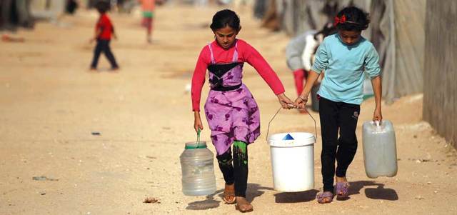 طفلتان سوريتان تحملان أواني مملوءة بالمياه في مخيم جرجناز جنوب إدلب.  رويترز