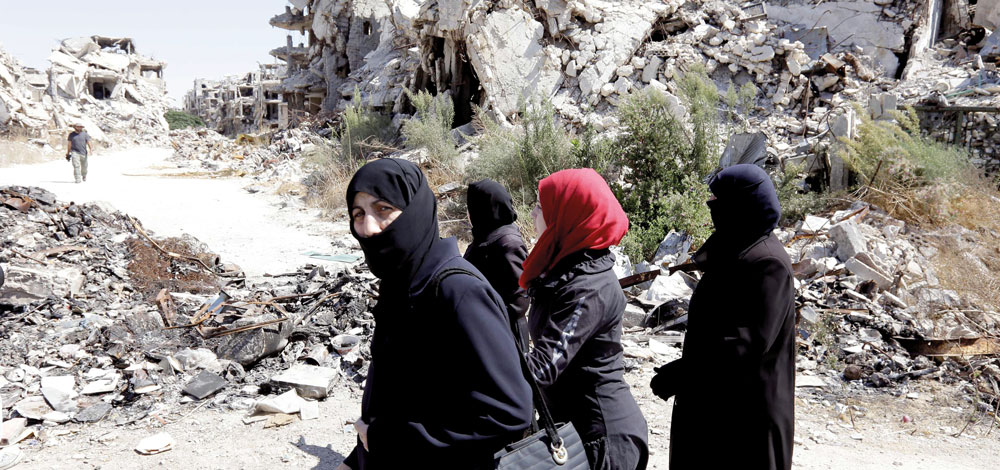 نساء يمشين بين المباني المدمرة في حي جورة الشياح بمدينة حمص الواقعة تحت سيطرة النظام. أ.ف.ب