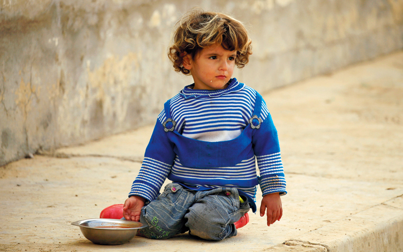 طفل يجلس على الرصيف لتناول الطعام في أحد  شوارع الموصل. رويترز