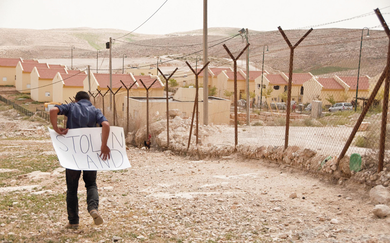 شاب يحمل لافتة مكتوباً عليها «أرض مسروقة» بالقرب من مستوطنة يهودية. أرشيفية