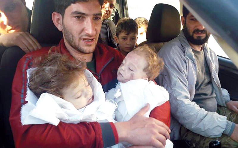 رجل يحمل طفليه التوأم بعد مقتلهما بالهجوم الكيماوي السوري. أ.ب