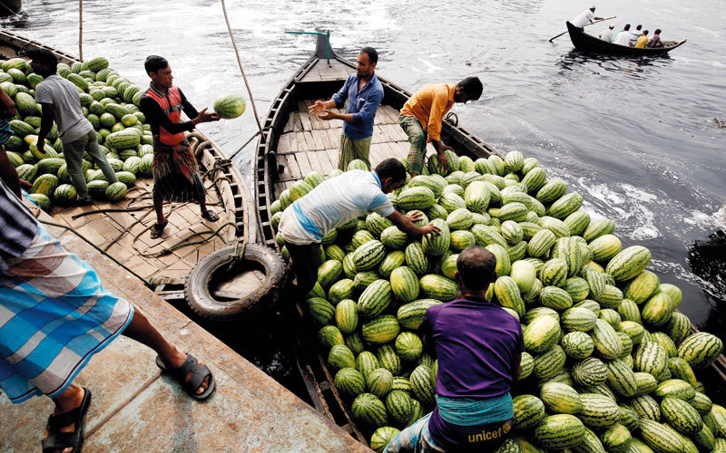 عمال بنغاليون يُحمِّلون قارباً بالبطيخ، لبيعه في سوق الفواكه بالجملة في العاصمة دكا. رويترز